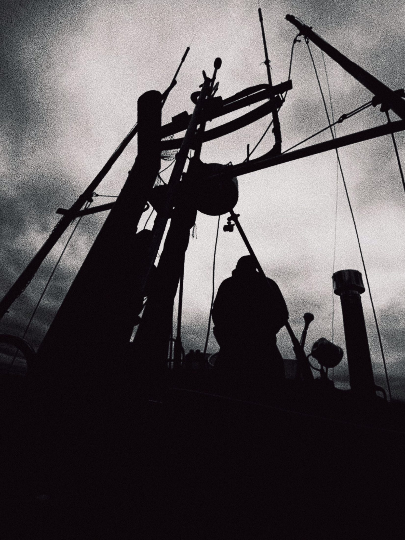 A figure on the mast of a boat against a storm sky